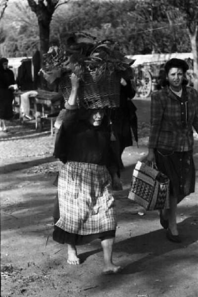 Portogallo. Cascais. Donna a piedi scalzi con cesto sulla testa di ritorno dal mercato - un'altra donna al suo fianco