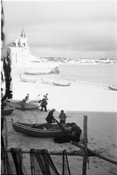 Portogallo. Cascais. Pescatori con le barche sulla spiaggia - in primo piano le reti appese - sullo sfondo il paese