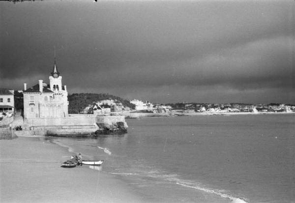 Portogallo. Cascais. Spiaggia con pescatori e barche - sullo sfondo il paese