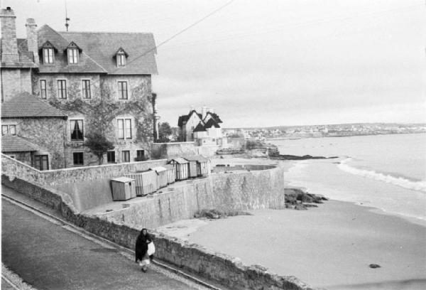 Portogallo. Cascais. Case e cabine a ridosso della spiaggia - mare - una anziana signora di passaggio sulla strada