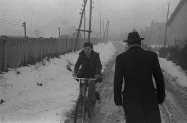 Donne in bicicletta e uomo lungo un sentiero innevato che corre a lato di una ferrovia