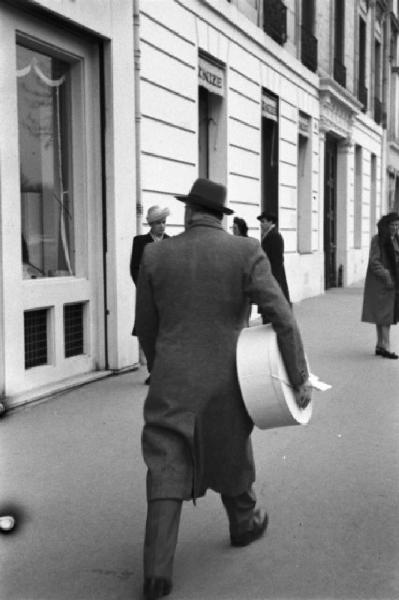 Parigi. Un uomo cammina lungo la strada portando sotto braccio una cappelliera
