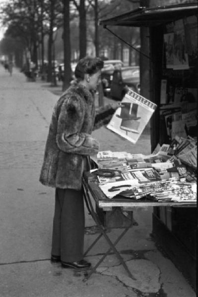 Parigi. Una donna con pelliccia acquista una rivista presso un'edicola