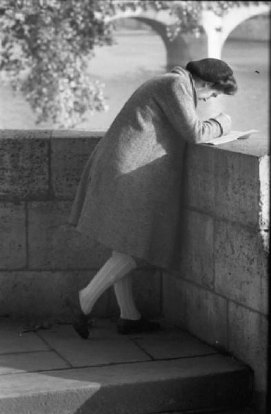 Parigi. Una ragazza legge un libro appoggiandosi a un muretto lungo la Senna