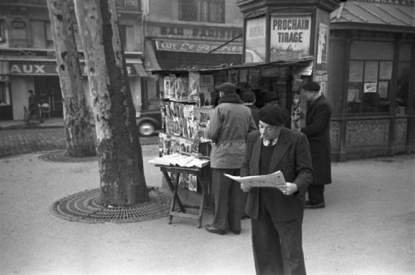 Parigi. Uomini in coda ad un'edicola. Un uomo legge il giornale