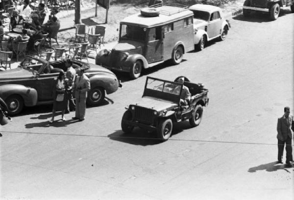 Italia Dopoguerra. Roma. Via Veneto. Jeep militare di passaggio - automobili lungo il marciapiede - tavolini di un bar all'aperto