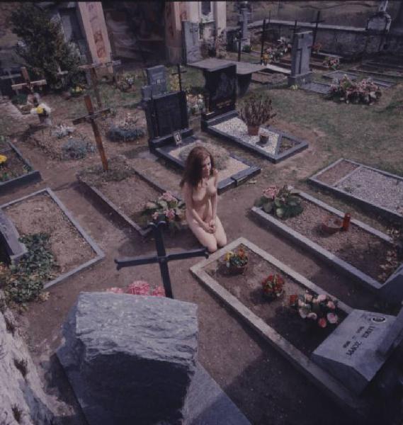 Nudo femminile in ginocchio davanti a una tomba all'interno di un cimitero