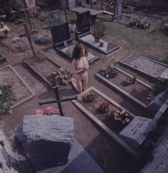 Nudo femminile in ginocchio davanti a una tomba all'interno di un cimitero