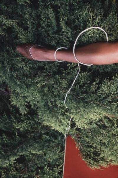 Gamba di donna con scarpa elegante nera con vegetazione sullo sfondo - la gamba è arrotolata da una corda