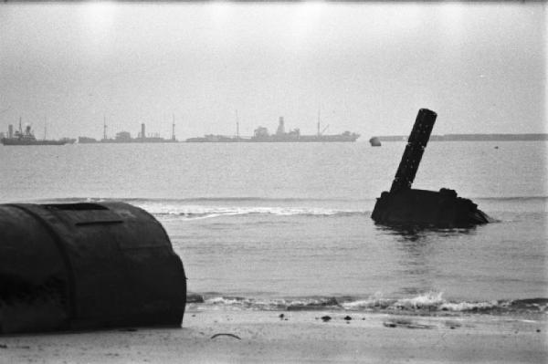 Normandia. Le spiaggie teatro dello sbarco alleato. Rottami di mezzi anfibi. Sullo sfondo navi da guerra