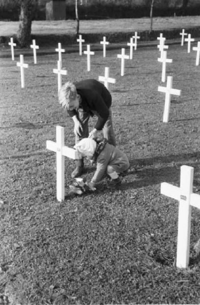 Normandia. St. Mère Eglise, cimitero di guerra. Due bambini del paese recano fiori a una croce in occasione di una commemorazione religiosa in memoria dei caduti dello sbarco alleato