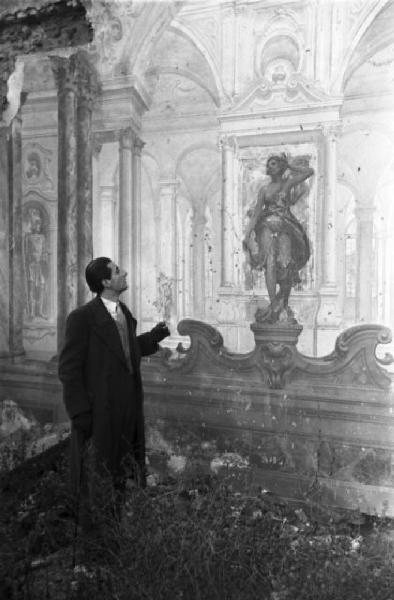 Italia Dopoguerra. Il pittore e architetto Fabrizio Clericisi posa tra le rovine di un palazzo bombardato indicando gli affreschi danneggiati