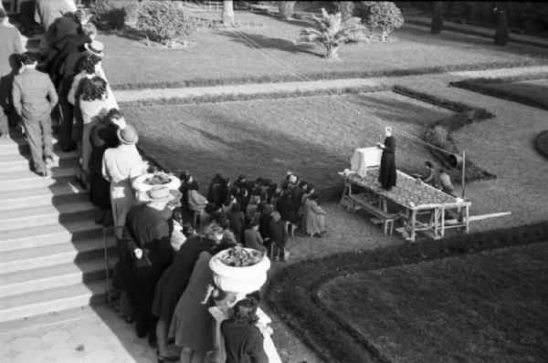 Genova Voltri. Celebrazione religiosa in occasione della Giornata della Serenità. Prete che officia davanti a un nutrito gruppo di donne mentre altre persone osservano dal parapetto di una scalinata