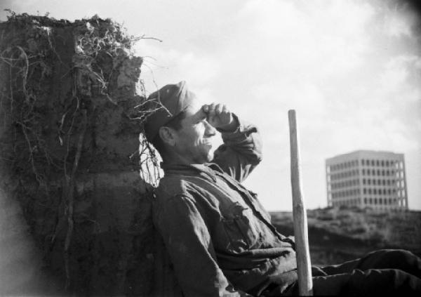 Italia Dopoguerra. Roma. Ponte sul Tevere in costruzione. Operaio munito di vanga in riposo. Sullo sfondo il Palazza della Civiltà e del Lavoro all'Eur