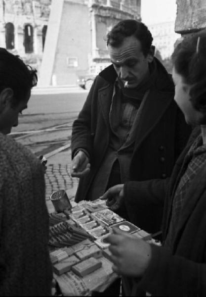 Italia Dopoguerra. Roma. Mercato nero. Vendita di sigarette all'angolo di una strada. Sullo sfondo il Colosseo