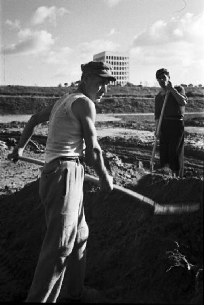 Italia Dopoguerra. Roma. Ponte sul Tevere in costruzione.  Operai che spalano. Sullo sfondo il Palazzo della Civiltà e del Lavoro all'Eur