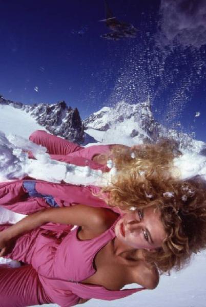 Campagna pubblicitaria Ellesse. Fotomodella indossa tuta da sci color fucsia - neve - modellino di aereoplano militare