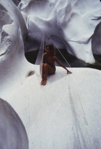 Nudo femminile - modella posa all'interno di una piramide in plexiglass posizionata su una roccia bianca e levigata