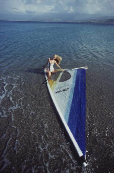 Campagna pubblicitaria Ellesse. Fotomodella indossa costume da bagno intero bianco -  vela di un windsurf