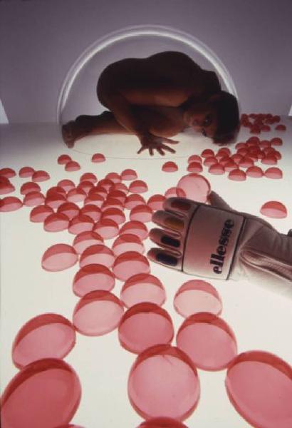 Nudo femminile -  modella in posizione fetale all'interno di una bolla di plexiglass. In primo piano bolle trasparenti rosse e un guanto da sci