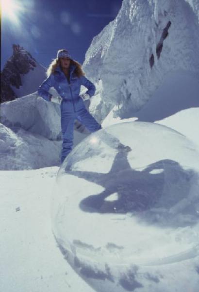 Campagna pubblicitaria Ellesse. Fotomodella indossa completo da sci azzurro - neve - sfera di plexiglass