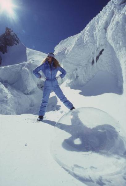 Campagna pubblicitaria Ellesse. Fotomodella indossa completo da sci azzurro - neve - sfera di plexiglass