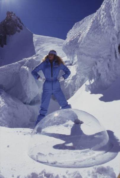 Campagna pubblicitaria Ellesse. Fotomodella indossa completo da sci azzurro - neve - sfera di plexiglass