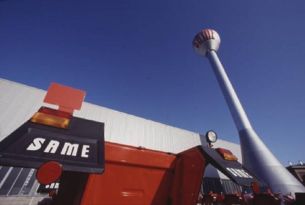 Gruppo SAME, stabilimento di Treviglio. Trattore agricolo - particolare dei posteriori; stabilimento sullo sfondo