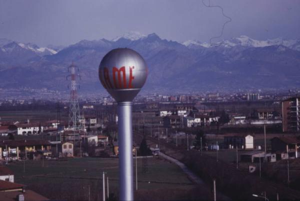 Gruppo SAME, stabilimento di Treviglio. Ripresa dall'alto dell'insegna aziendale sorretta da un'altissima struttura a colonna. Sullo sfondo il paesaggio circostante