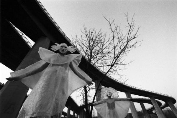 Due figure mascherate con abiti in pluriball nei pressi di un cavalcavia della tangenziale