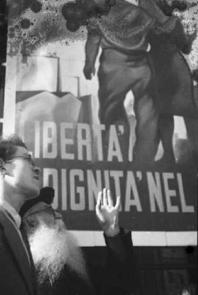 Milano. Due persone discutono sullo sfondo di un manifetso propagandistico recante la scritta "LIBERTA' DIGNITA' NEL"