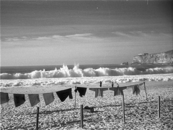 Nazaré. Bancheria stesa ad asciugare in spiaggia - sullo sfondo onde che frangono
