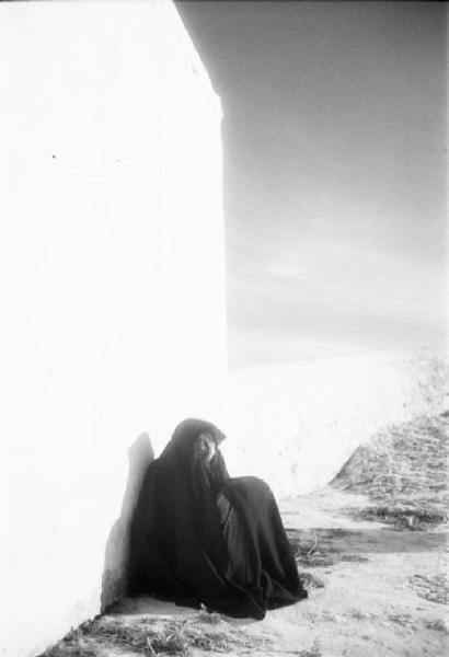 Nazaré - donna lusitana avvolta in un manto nero siede appoggiata a un muro