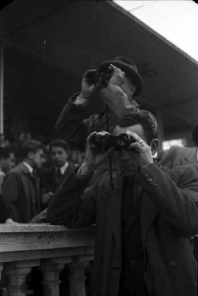 Italia Dopoguerra. Milano. Ippodromo di San Siro - Gran Premio. Coppia di spettatori con binocolo segue la corsa