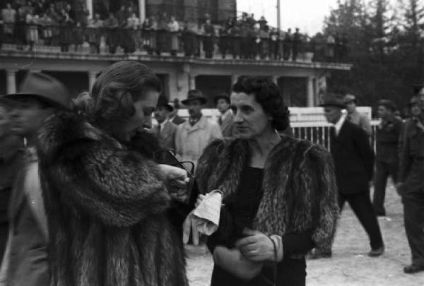 Italia Dopoguerra. Milano. Ippodromo di San Siro - Gran Premio. Due donne conversano tra i passanti