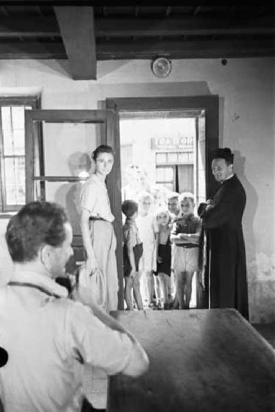 Italia Dopoguerra. Sant'Angelo Lodigiano. Reportage sulla figura di Santa Francesca Cabrini - Federico Patellani all'interno di un oratorio circondato dal prevosto e da un gruppo di fanciulli