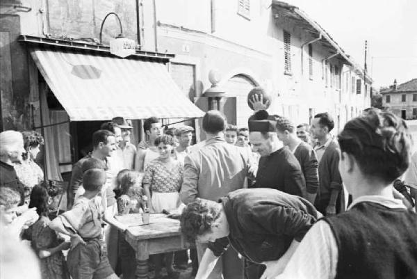 Italia Dopoguerra. Sant'Angelo Lodigiano. Reportage sulla figura di Santa Francesca Cabrini - il parroco nelle strade del paese circondato dagli abitanti