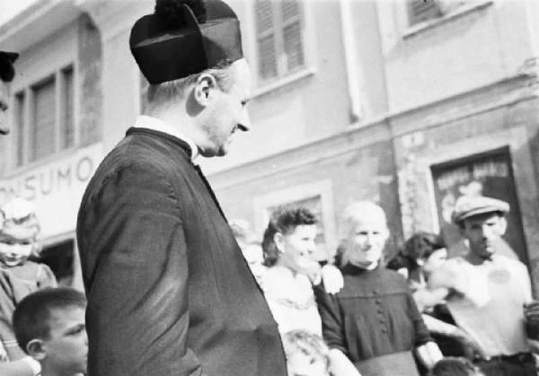 Italia Dopoguerra. Sant'Angelo Lodigiano. Reportage sulla figura di Santa Francesca Cabrini - un momento di vita del paese - in primo piano il parroco circondato dai cittadini