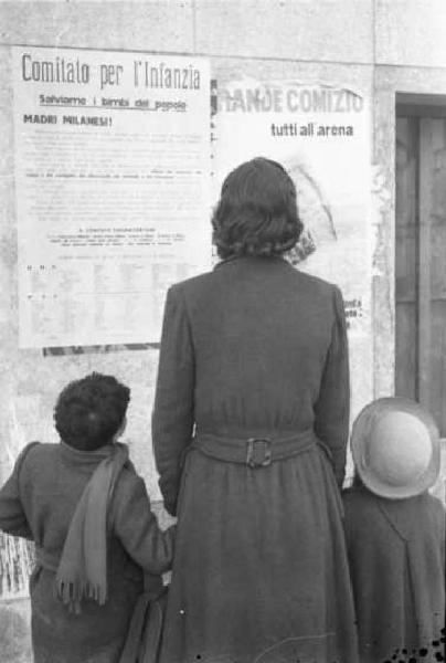 Milano dopoguerra. Signora con bambini di fronte a un manifesto del "comitato per l'infanzia"