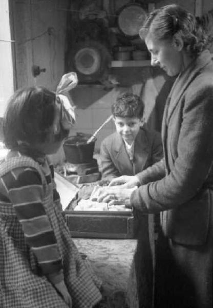 Milano dopoguerra. Signora in cucina con due bambini che la osservano