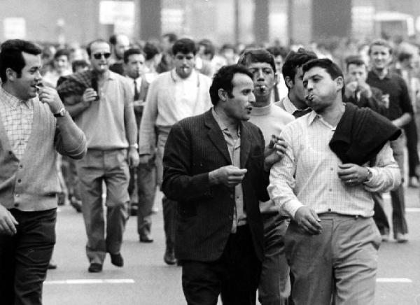 Milano. Manifestazione sindacale. Due manifestanti chiacchierano fra loro - un terzo li ascolta - sullo sfondo il corteo