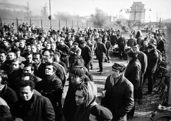 Milano. Manifestazione con serrata degli stabilimeti Autobianchi. Manifestanti ascoltano un comizio [?] - sullo sfondo i cancelli della ditta e rifiuti in fiamme