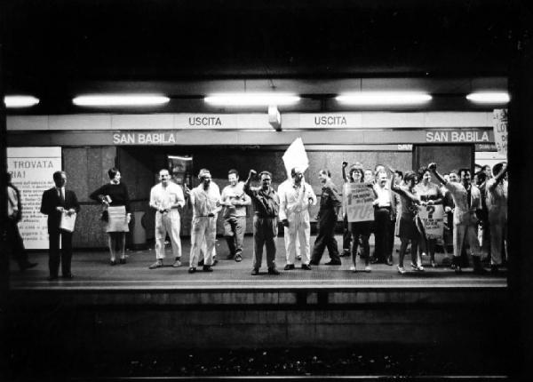 Milano. Fermata della metropolitana San Babila. Banchina. Manifestanti della Pirelli in tuta da lavoro esibiscono cartelli con slogan di protesta e alzano il pugno in segno di lotta - alcuni passeggeri li osservano