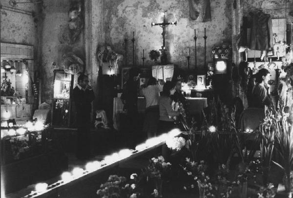 Culto ritualizzato dei morti. Napoli - Cimitero delle Fontanelle, interno [?] - Devoti davanti a pareti con ex-voto - Fiori e lumini