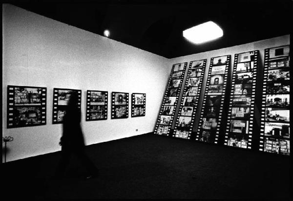 Galleria d'arte - Mostra fotografica di Aldo Tagliaferro - Visitatore in movimento al centro della sala - Alle pareti le immagini montate in striscia