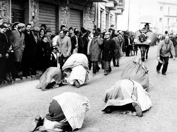 Carnevale. Mascherata - astanti osservano persone travestite e inginocchiate