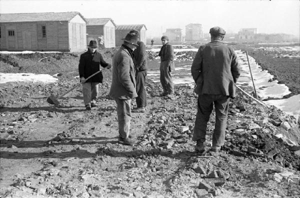 Italia Dopoguerra. Milano - Quartiere Baggio - Periferia - Edifici prefabbricati in legno - Cantiere - Terreno sterrato - Uomini con pala