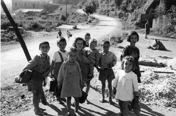 Italia Dopoguerra: Valmontone bombardata. Valmontone - Ritratto di gruppo: bambini con cartelle di scuola lungo una strada sterrata