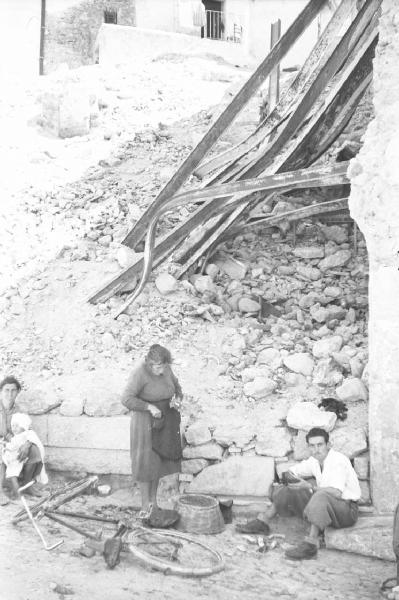 Italia Dopoguerra: Valmontone bombardata. Valmontone - Strada - Macerie - Ritratto di gruppo: donna con bambino in braccio, anziana e uomo seduto su un gradino - Bicicletta a terra