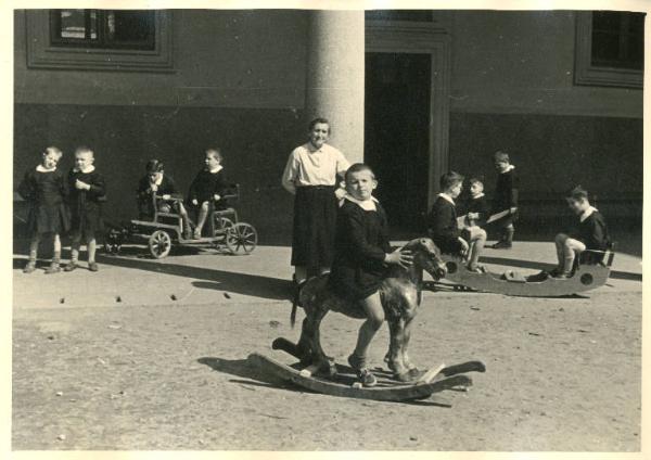 Istituto dei Ciechi di Milano - Scuola elementare - Cortile - Ricreazione - Bambini giocano con un dondolo, un cavallo a dondolo, una macchinina - Maestra